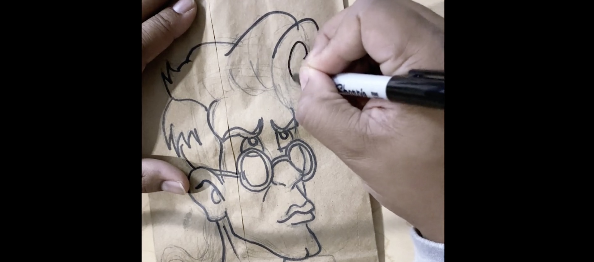 The hands of artist Alexander Chisley drawing one of the Real Ghostbusters in Sharpie over a pencil sketch on a brown paper bag