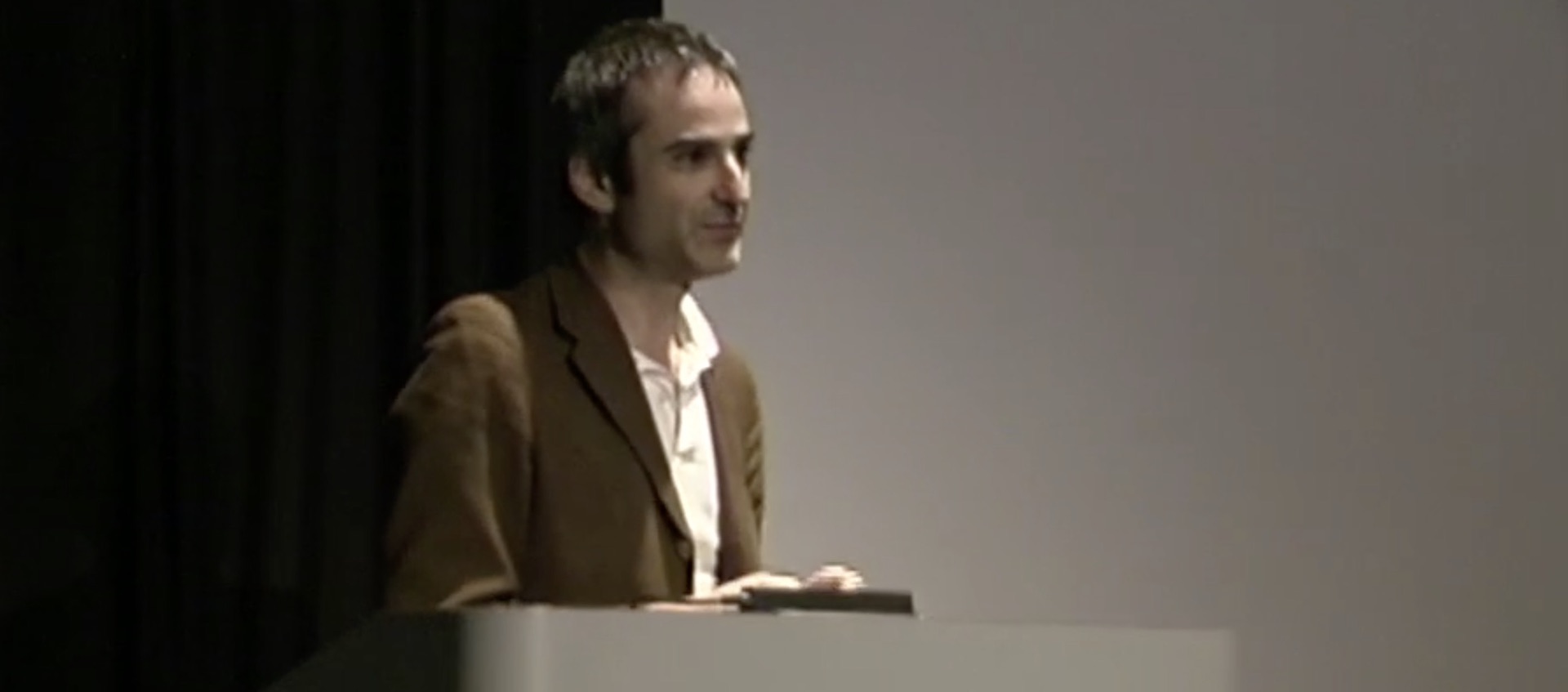 Filmmaker Olivier Assayas speaking from the podium on the stage of the Film/Video Theater at the Wexner Center for the Arts