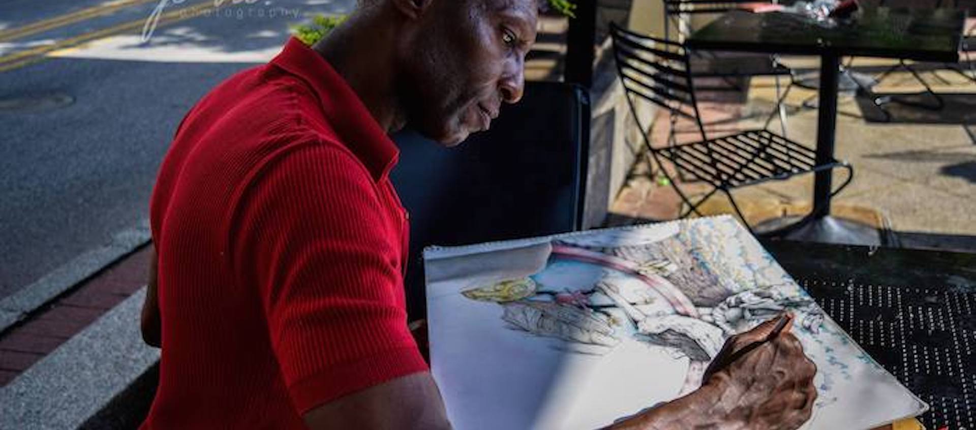 Columbus artist Michael Hodges sits at a table outside drawing