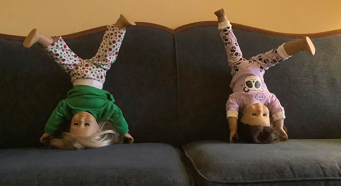 A color film still that shows two dolls doing handstands on a gray couch