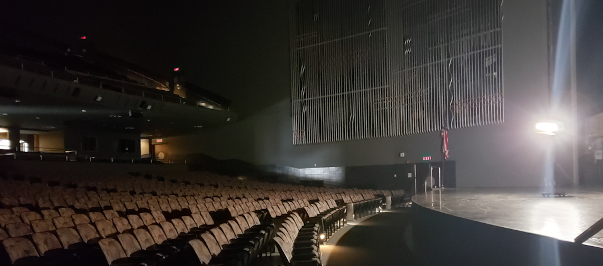 A side view of an empty Mershon Auditorium lit by a single bare bulb lamp on stage