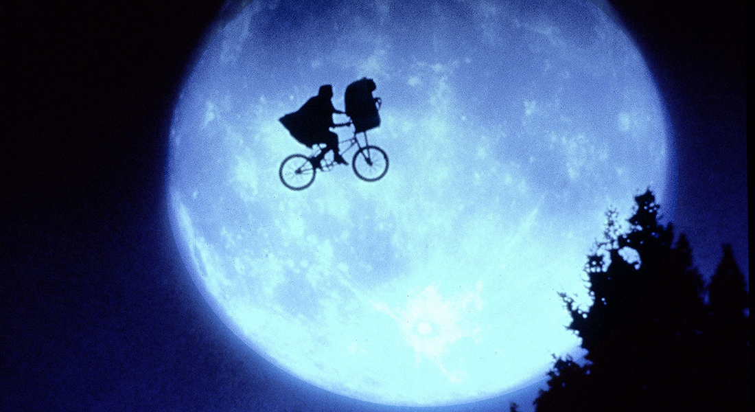 A child rides a BMX bike through the air; he's shown in silhouette against a full moon that fills the sky