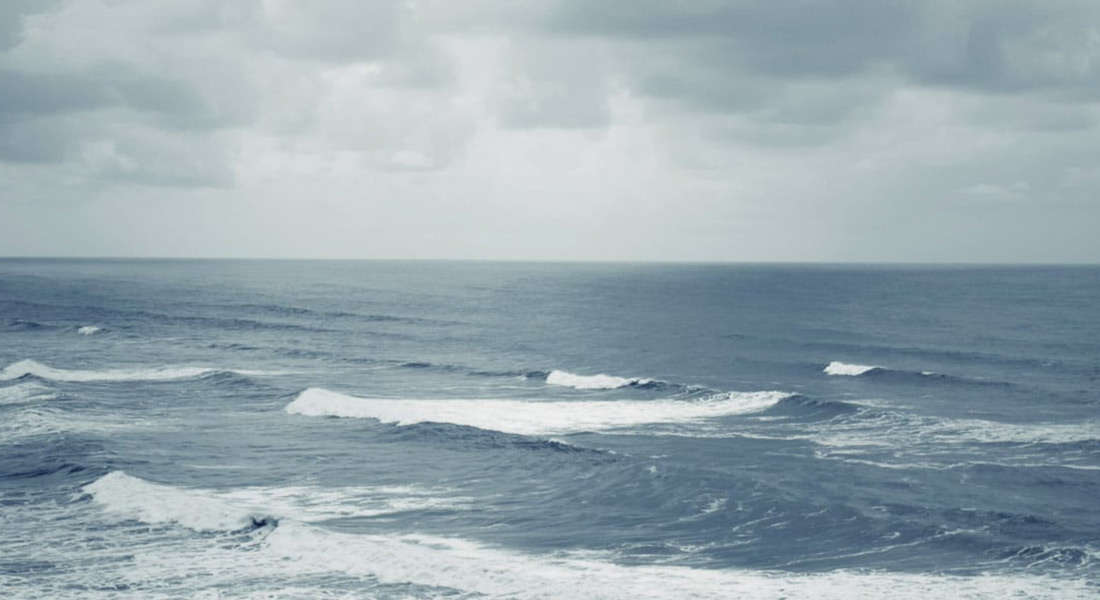 The view of the ocean on a cloudy day; small waves break, traveling from right to left