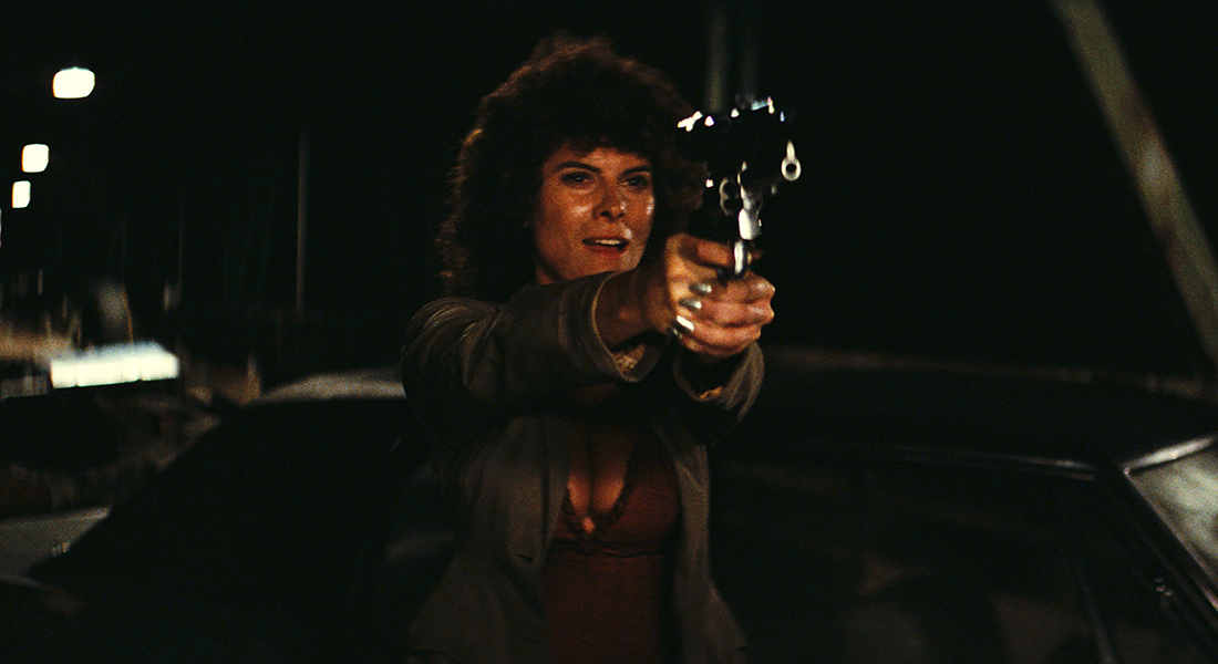 A woman on a bridge points a large handgun at the camera