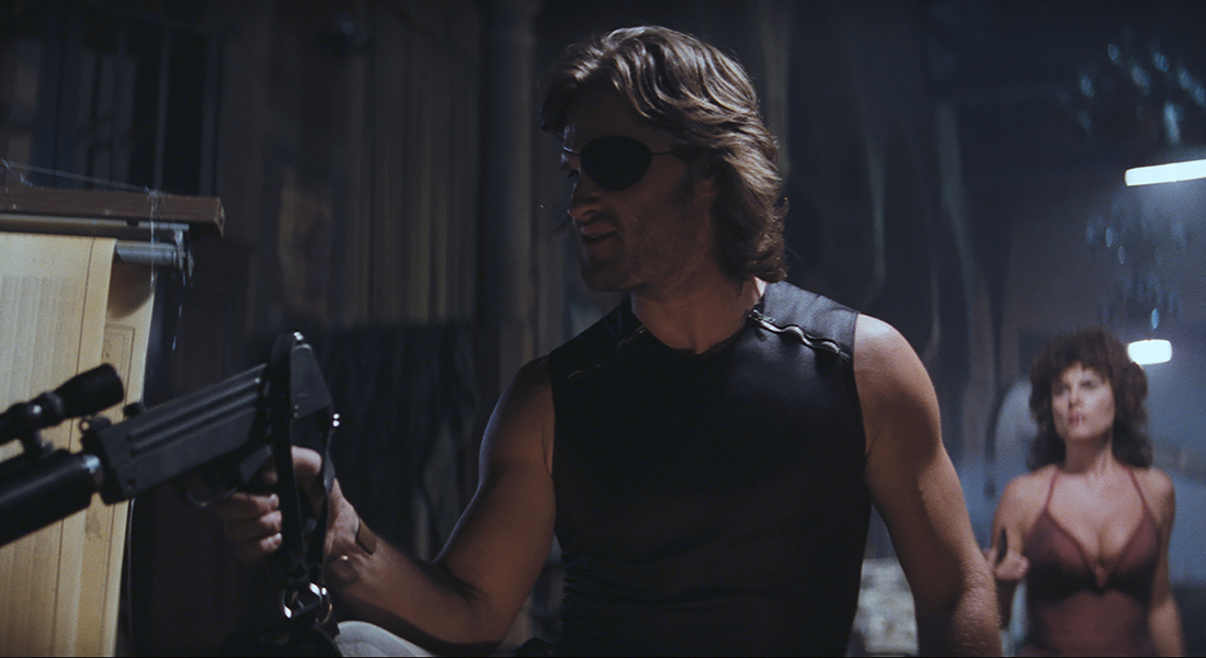 A man with an eyepatch handles a modified gun while someone looks on from the back of the same room