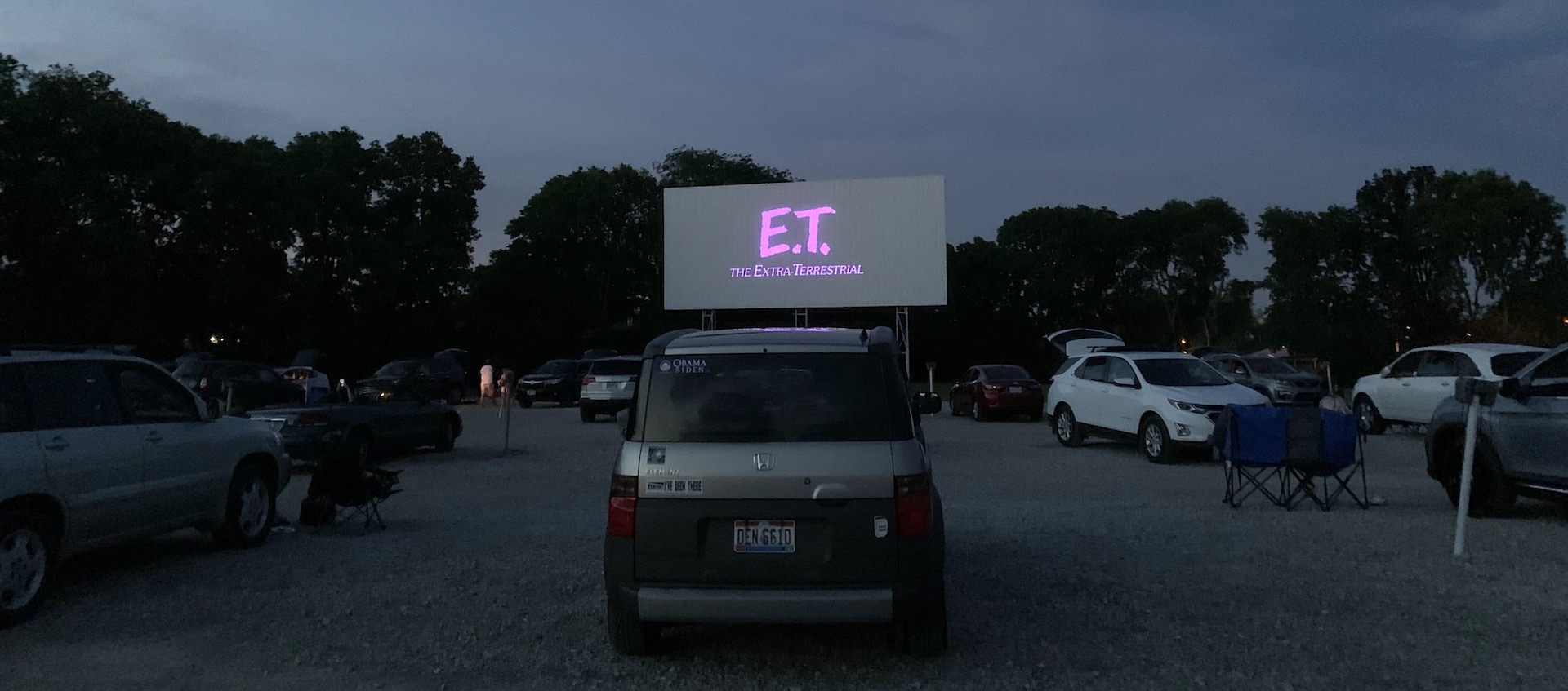 Cars in front of a drive-in screen with the opening credit for E.T.: the Extra-terrestrial