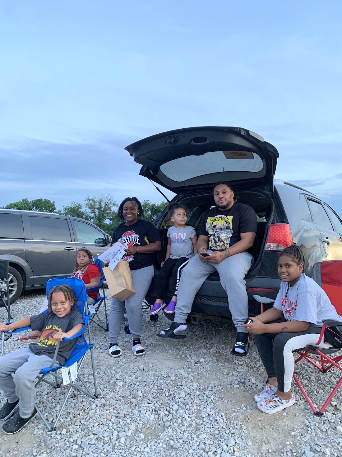 A family of two parents and three young kids sitting in the open back of a van at the drive-in