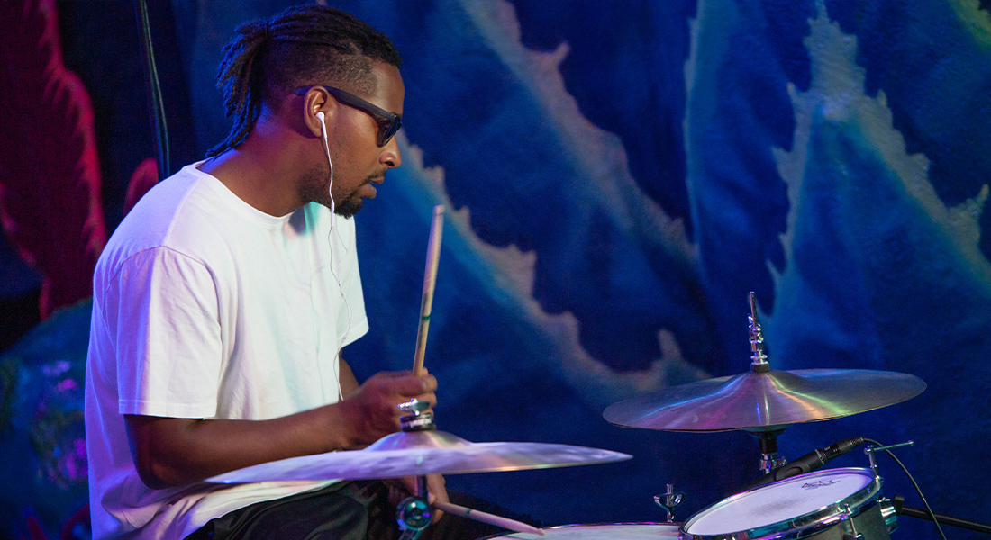 A person in a white t-shirt and sunglasses playing drums