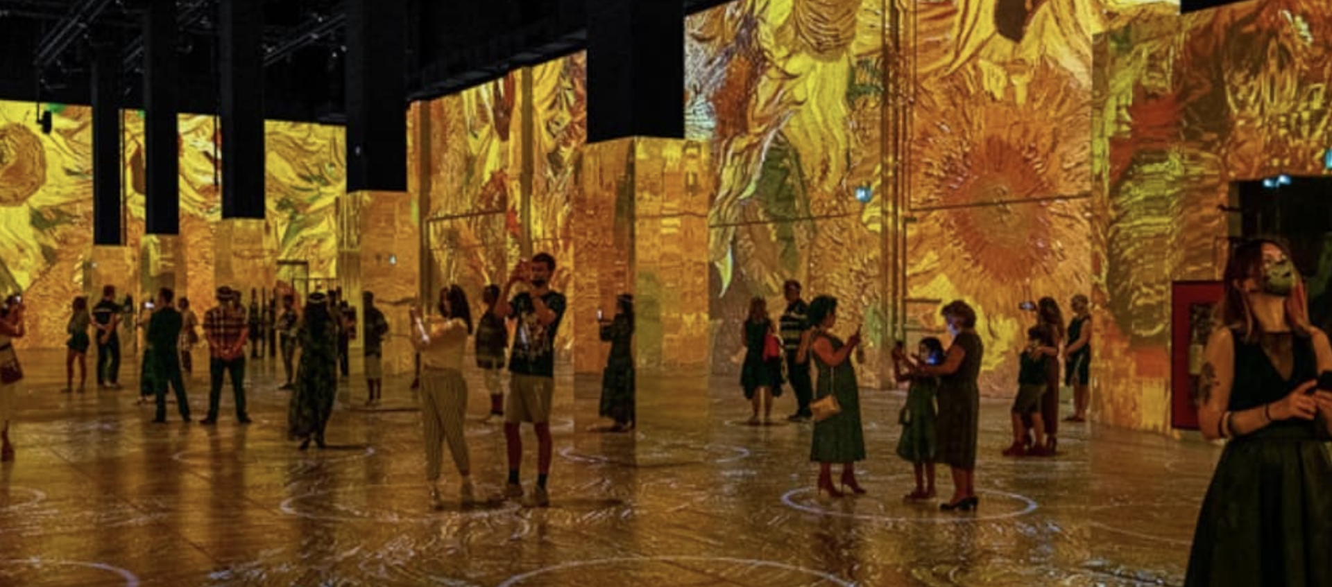 An image of the touring Van Gogh installation. A soft focus image of people in a gallery surrounded by paintings