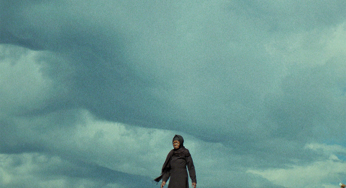 A person in a dark set of robes stands in front of a vast, cloudy skyline