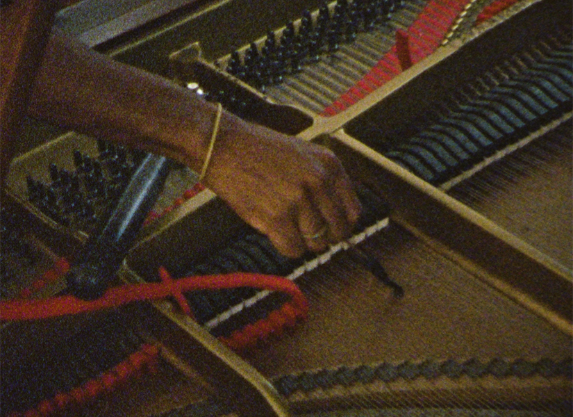 A close-up of a hand repairing a string in side of a piano