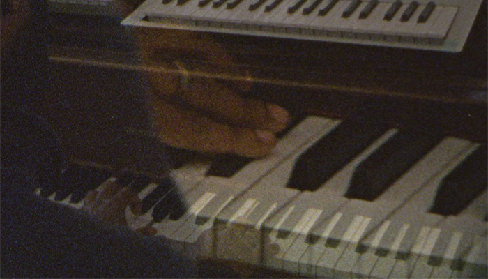 A close-up of piano keys with a ghostly image of hands touching the keys