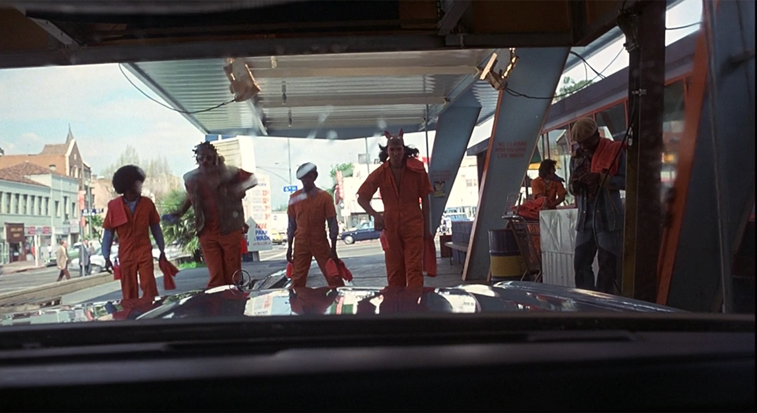 A view from inside of a car in car wash looking at four people in worksuits standing in front of the car's windshield