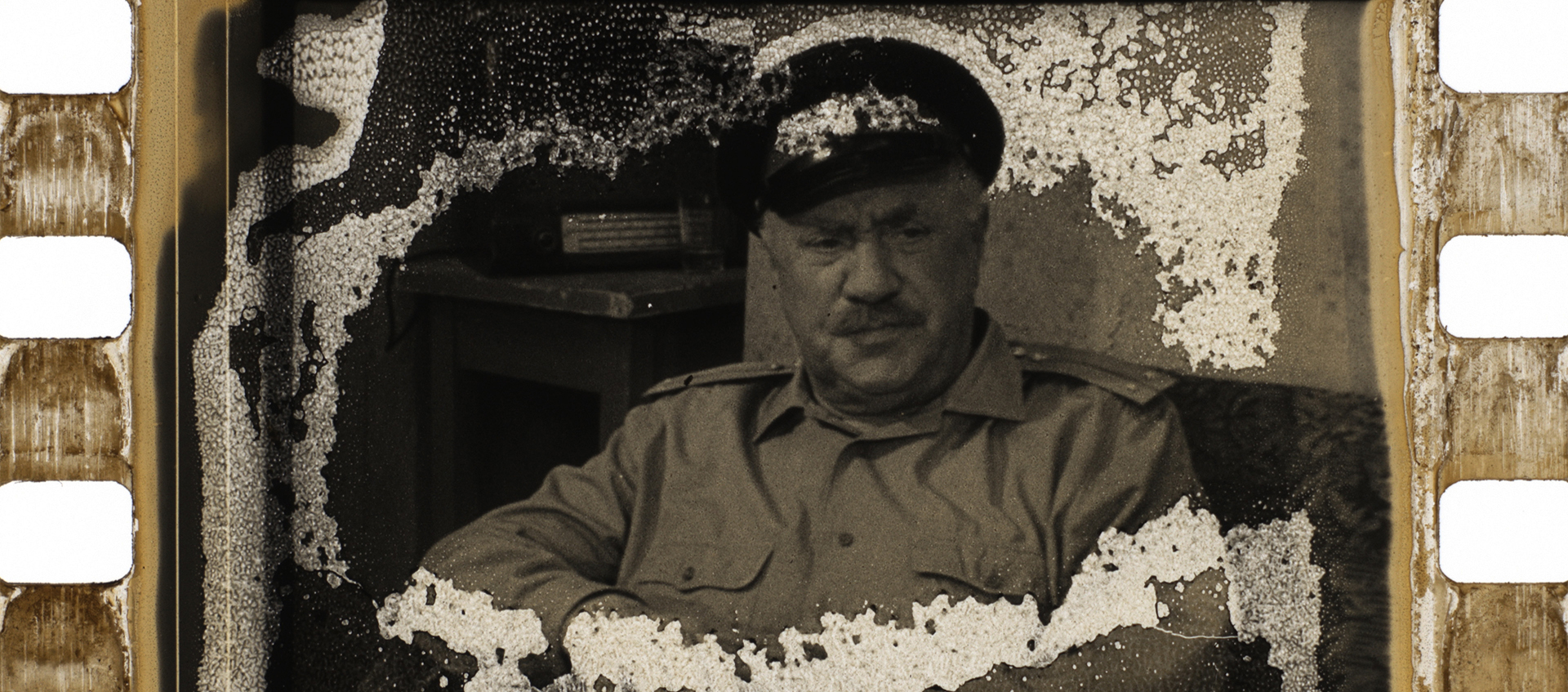 A deteriorating strip of film with an image of a man in a hat burned onto it