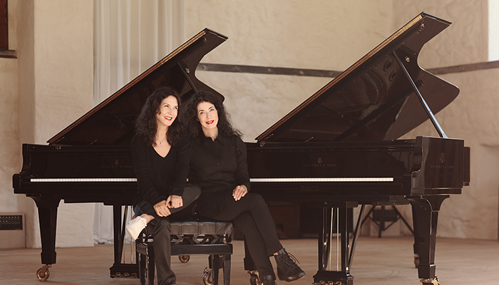 The Labèque Sisters seated in front of two pianos