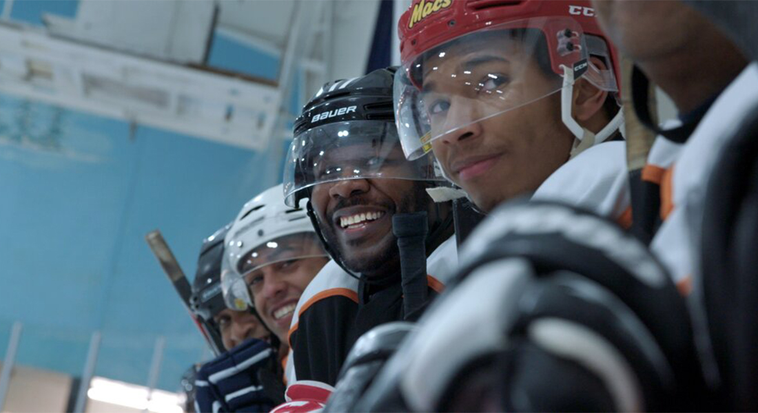 A row of four Black Canadian teens in hockey gear smile at the camera in this documentary still.