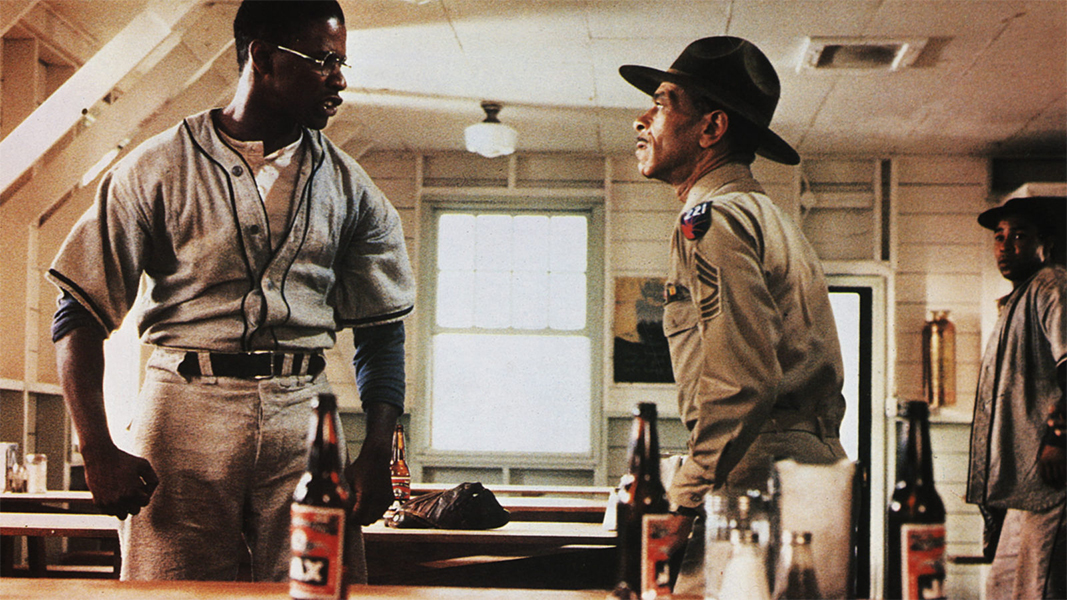 Denzel Washington in jeans and gray shirt, wearing eyeglasses stands in front of a military officer and is telling at him