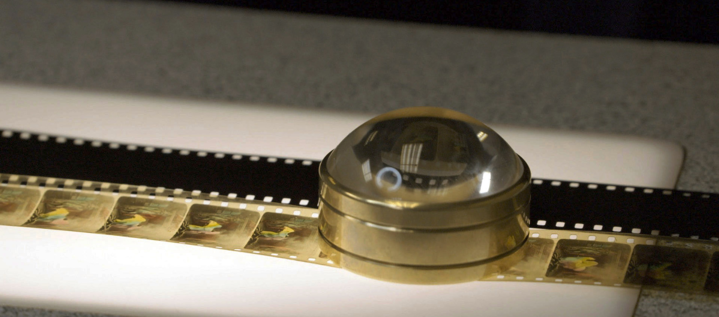 An image of a film strip on a light table with a magnifying glass laying on top of it