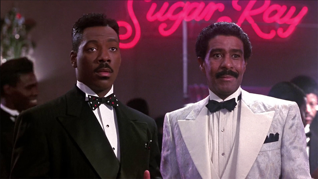 Eddie Murphy and Richard Pryor stand in front of a neon sign that says Sugar Ray