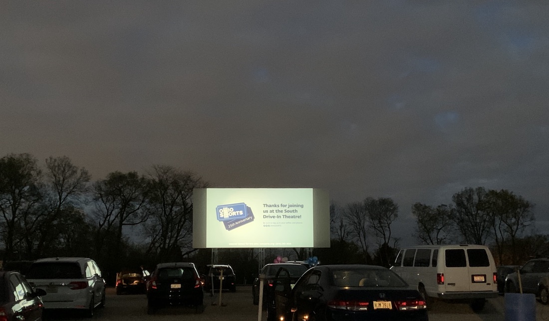 Parked cars facing a screen at South Drive-In with an Ohio Shorts graphic projected on it