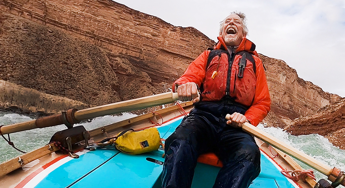 A person rowing a kayak along rapids throws their head back in joy