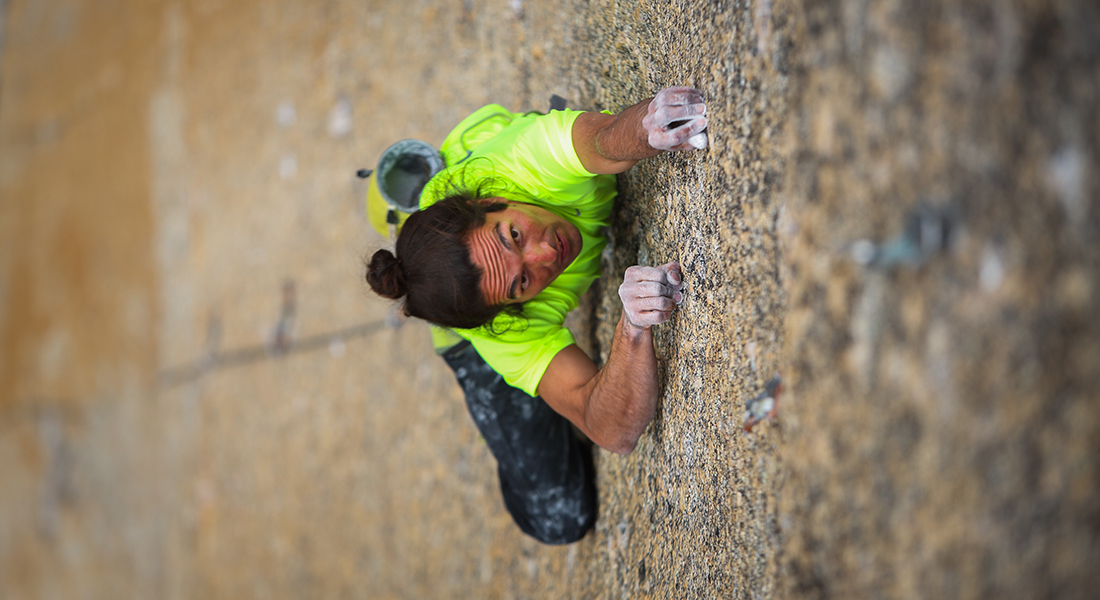 A person in a bright neon green shirt climbs the side of a mountain