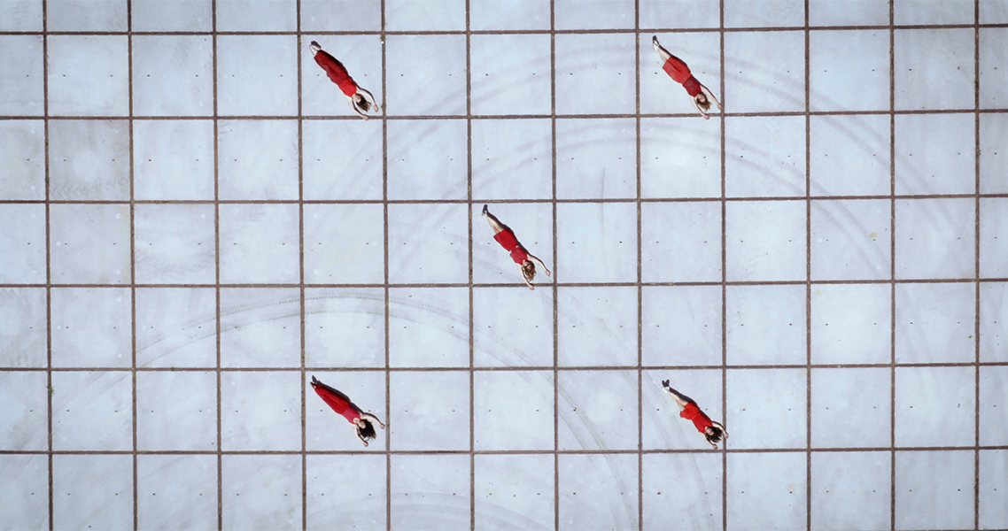 An overhead view of five women in red spaced evenly across a grid-like stone plaza.