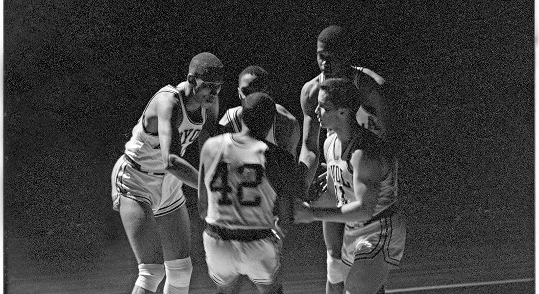 A group of five basketball players gather in a circle