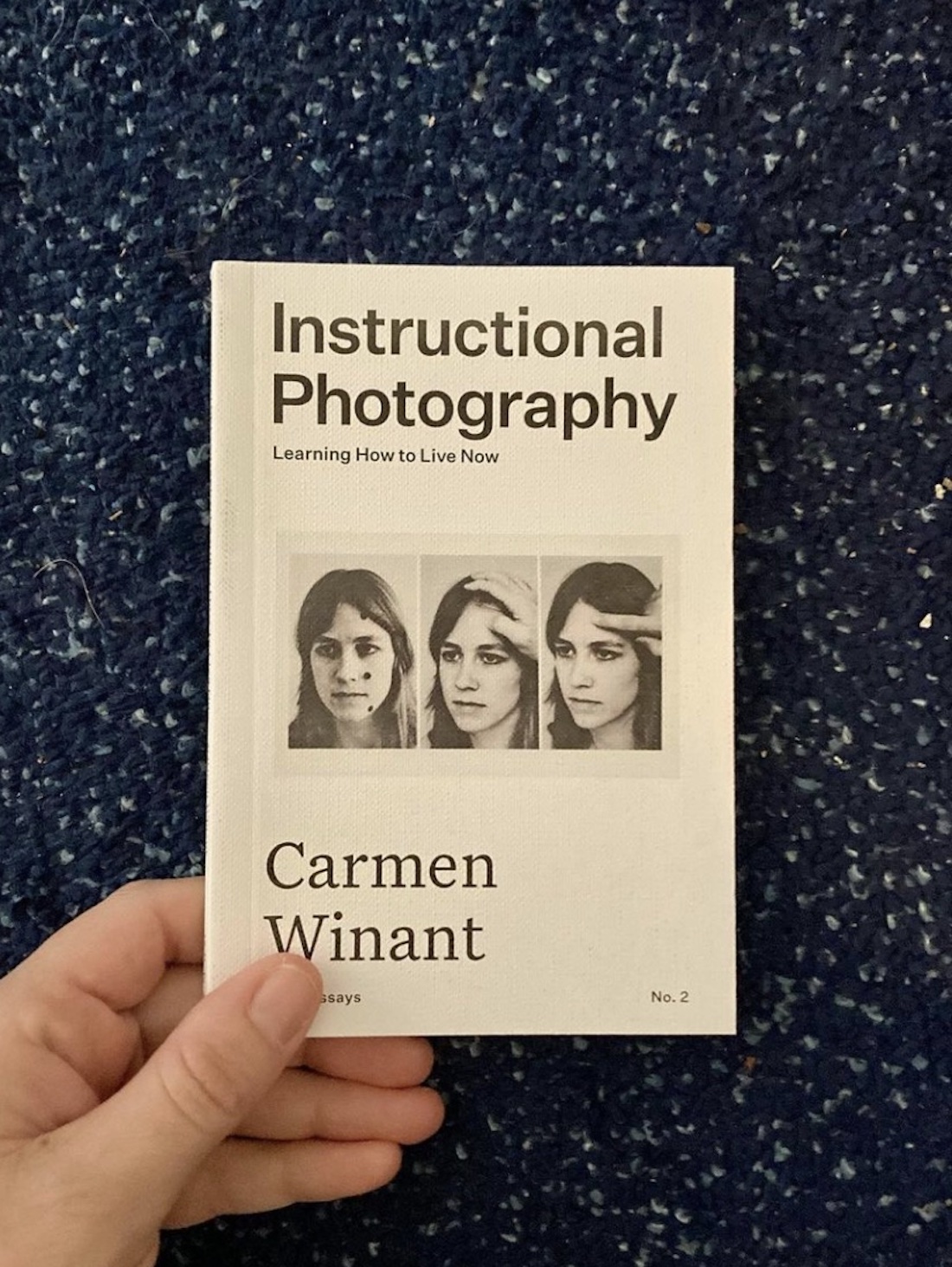 A hand holding a copy of Carmen Winant's book Instructional Photography