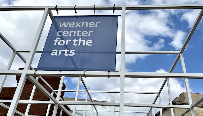 A banner reading "wexner center for the arts" installed on the exterior steel grid that lines one side the center building