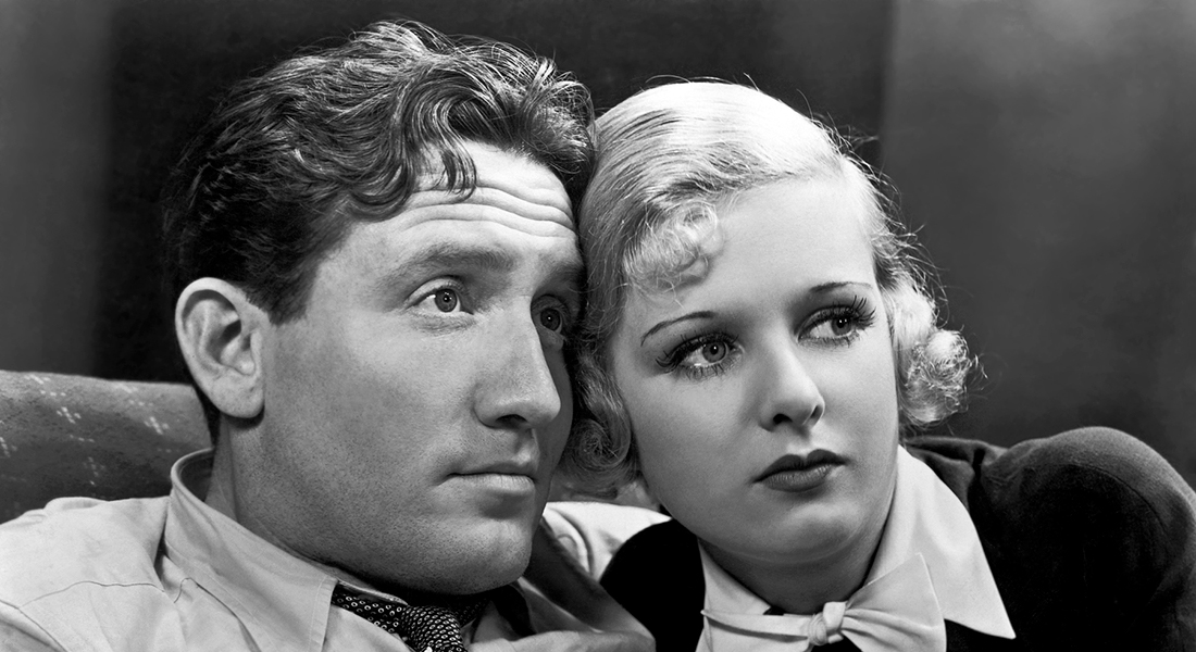 Black-and-white still from Me and My Gal featuring a man with curly, darker hair who has distinct lines on his forehead and is wearing a button-down shirt and patterned tie. Next to him (on the right) is a woman with short, curly blonde hair; she has her hand on the man’s chest and a ring on her finger, and she’s wearing a black shirt with a white collar and bowtie.
