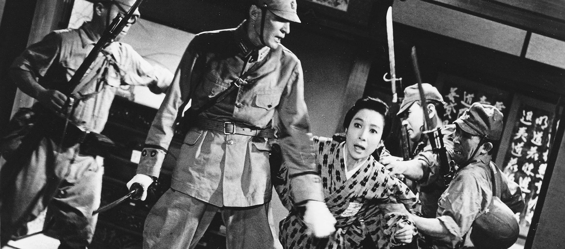 Black-and-white still of a person in a patterned kimono who is trying to flee from four soldiers with weapons.