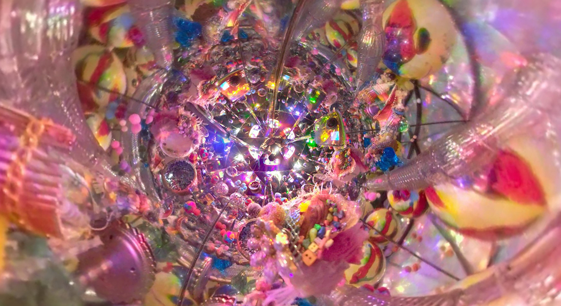 Still of what appears to be the inside of a kaleidoscope featuring multicolored balls, toys, and trinkets with lots of pink shades