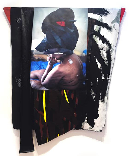 The Unknown One by artist Jasmine Murrell features a photograph of a seated, nude Black woman wearing a headdress composed of folded black vinyl records with red, blue, and white labels distributed throughout it. The photo is centered on a multicolored and irregular-shaped tapestry that is hung on a white wall.