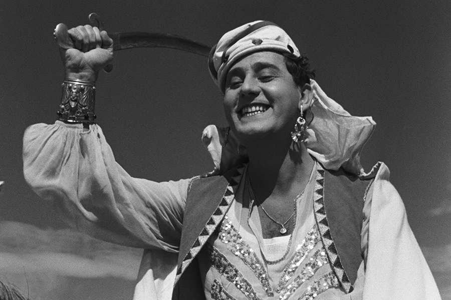Black-and-white still from The White Sheik featuring Fernando (Alberto Sordin) smiling, wearing a Sheik headdress and clothing, and holding a sword above his head.