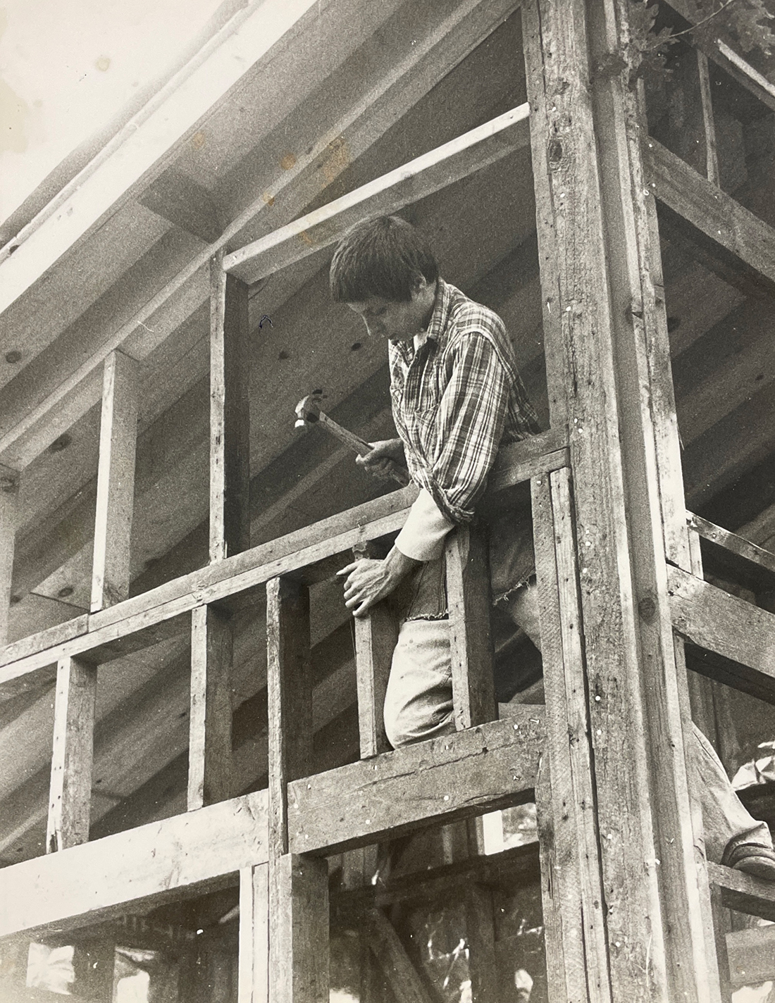 Black-and-white photograph of a woman using a hammer to fasten studs to the frame of a cabin