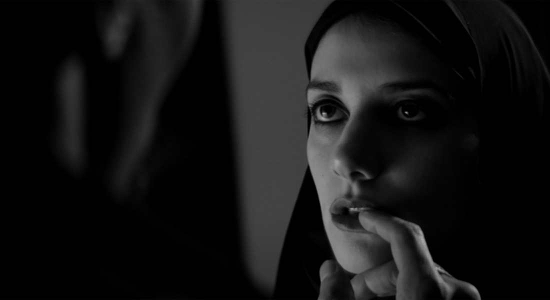 The Girl looking into the distance and wearing a dark chador. The left side of the image is blacked out due to someone is standing in front of the Girl. The unknown person’s finger is touching the Girl’s bottom lip.