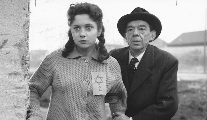 A scene from the 1960 Yugoslavian film Deveti Krug in which an elderly man holds the arm of a young woman with a Star of David symbol pinned to her sweater as they look intensely at something ahead