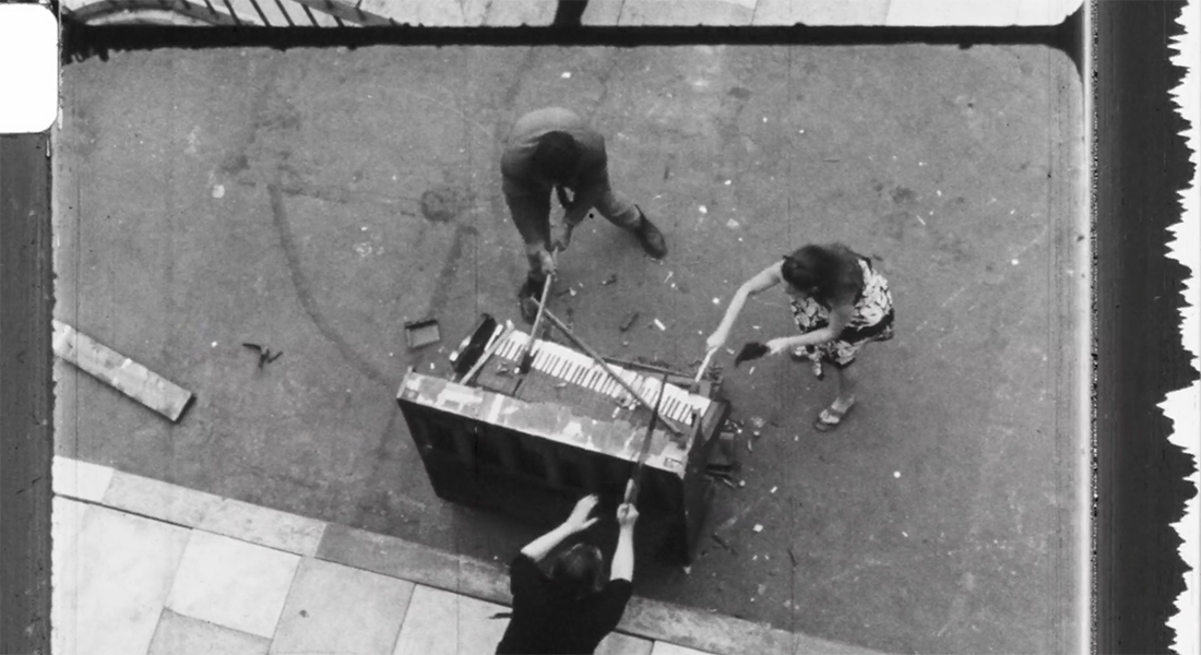 An overhead image of three people destroying a piano on a street