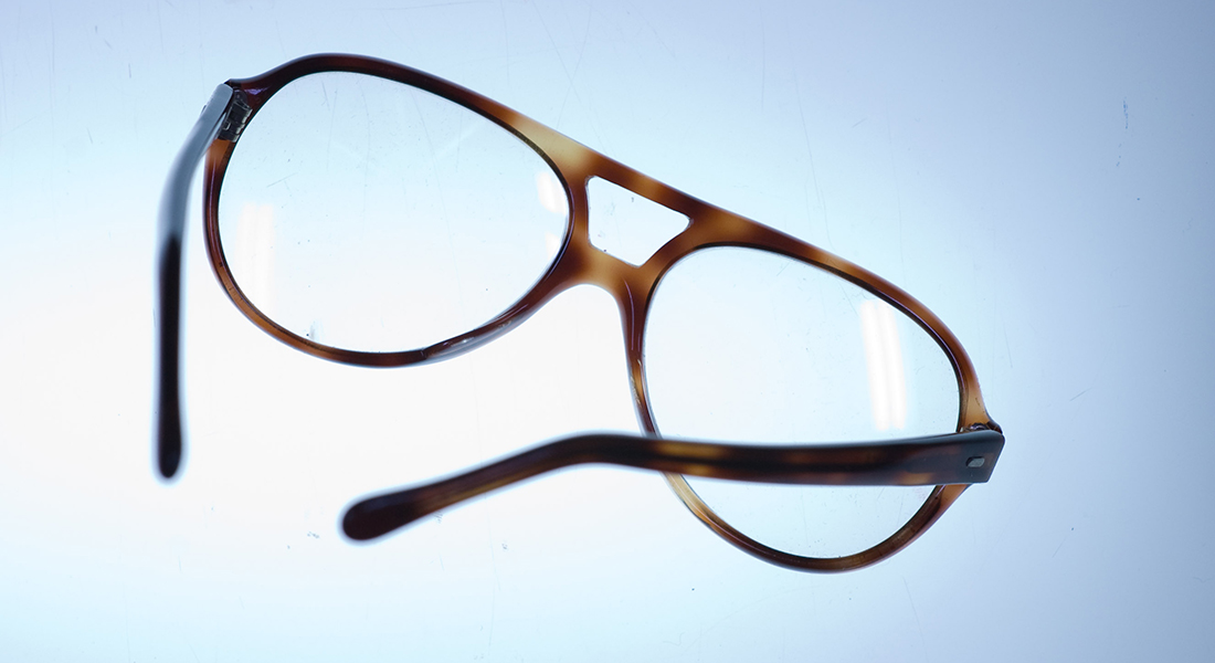 Clear glasses with brown frames against a light blue background lit with bright light.