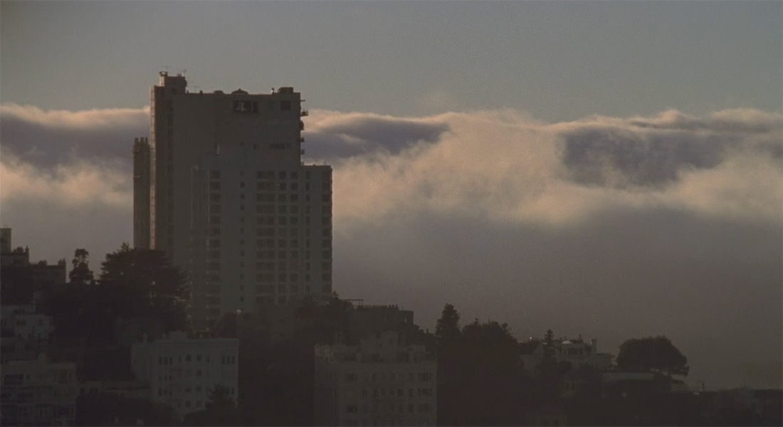A building towering in the sky in front of a mass of cloud cover starting to envelop it.