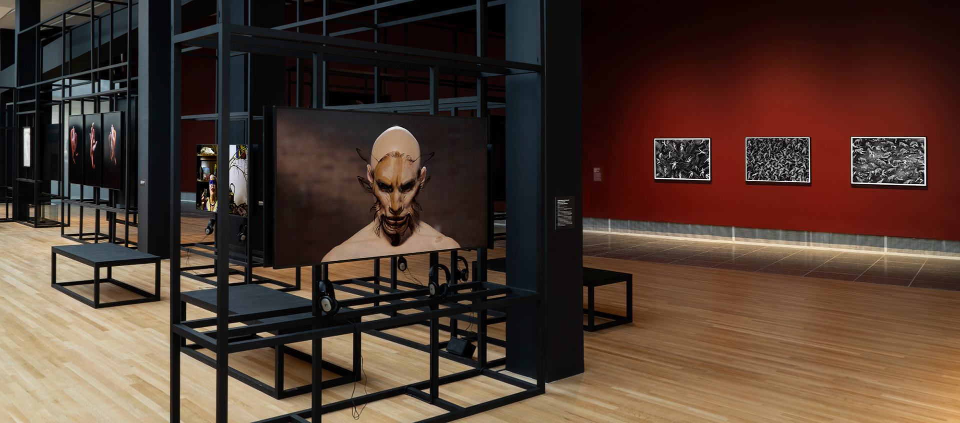 Gallery with burgundy walls and black scaffolding structure that displays monitors and photographs.