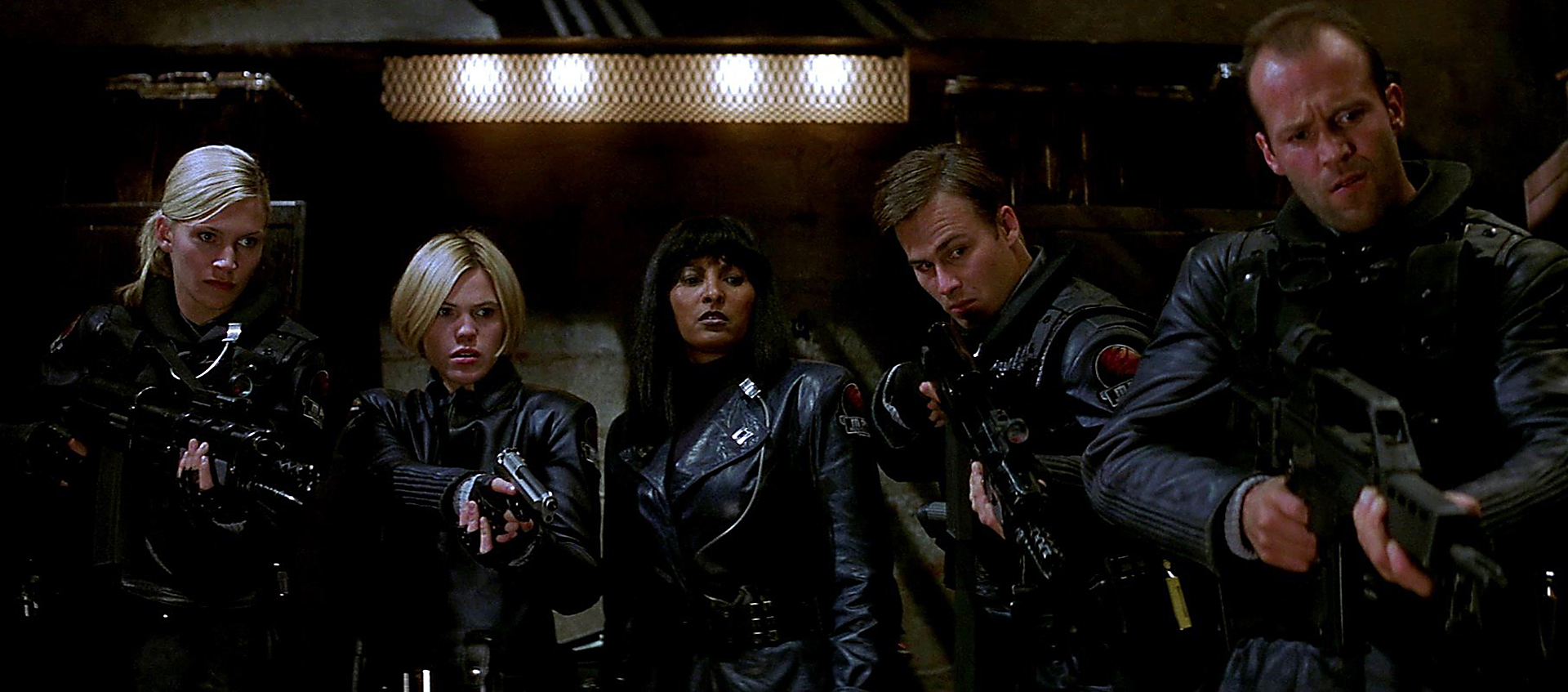 Five guntoting futuristic cops in black uniforms all stand point guns at something just out of view. Pam Grief stands in the center.