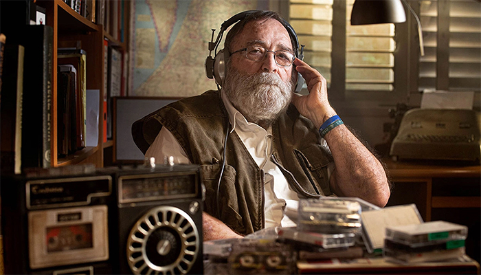 a man seated at a desk with headphones one, and a radio in foreground