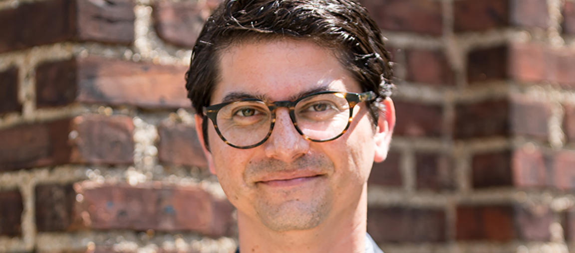 Headshot of Paul Farber, who has short dark hair and light skin, wearing glasses and smiling in front of a brick wall.