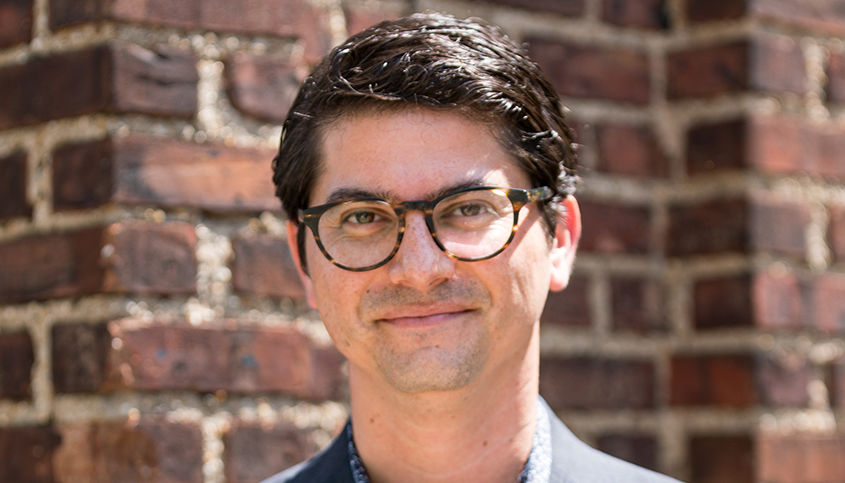 Headshot of Paul Farber, who has short dark hair and light skin, wearing glasses and smiling in front of a brick wall.