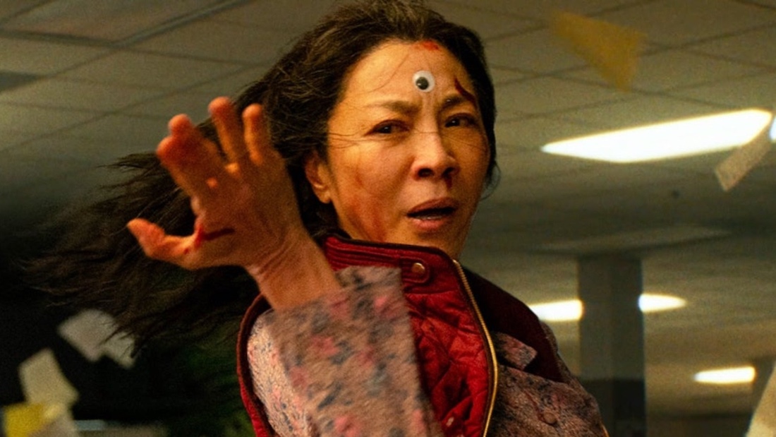 Actress Michelle Yeoh, wearing a googly eye at the center of her forehead like a third eye, assuming a fighting pose in a still from the film Everything Everywhere All at Once