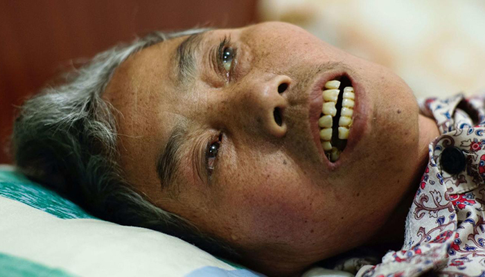 A close-up image of Mrs. Fang, a Chinese person who is close to death. Her head rests against a pillow, and her mouth is slightly open.