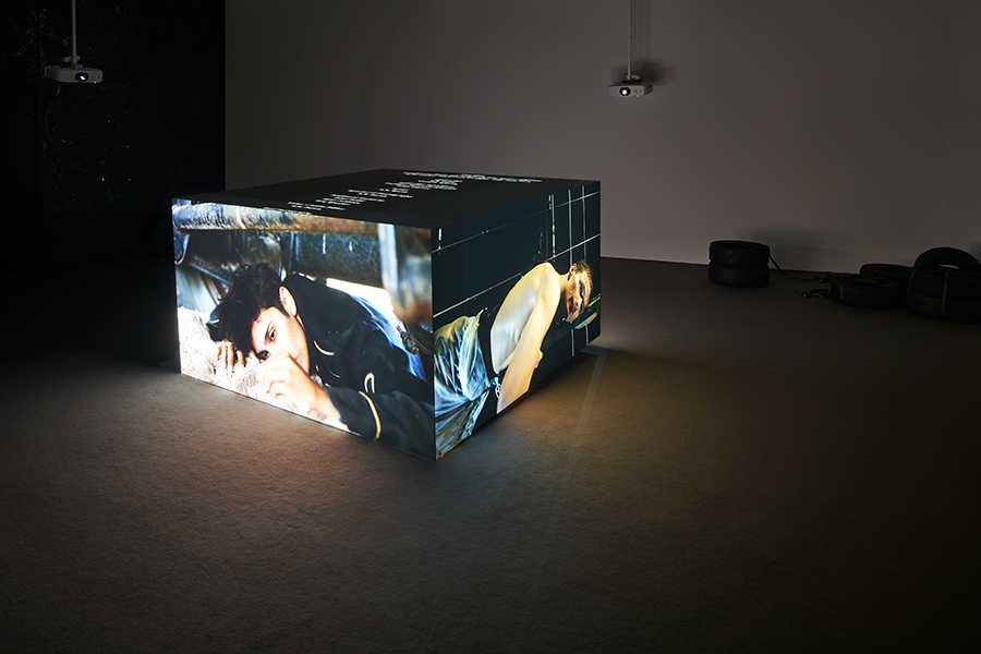 A cube with different video channels projected on each side lights up a dark room.