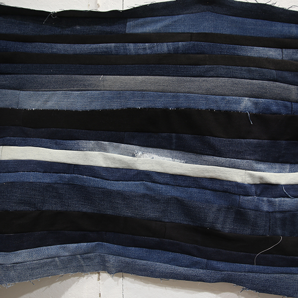 Close-up of a long horizontal strip of blue, black, and white denim fabric sewn together.